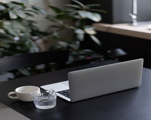 An organized lit home office desk setup with a laptop and a clear glass of water near a window